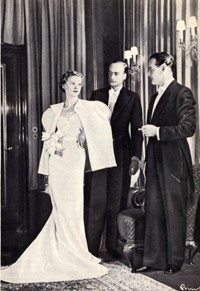 Dáma a gentlemani v nejslavnostnějším oděvu: žena ve velké večerní toaletě s pláštěnkou a bohatou dekorací z umělých tulipánů, pánové ve fracích, časopis Eva, r. IX, č. 5, 15. 1. 1935