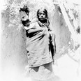 Žena s dítětem na zádech stojící před zdí domu, Hopiové z puebla Walpi. USA, Arizona, 1900