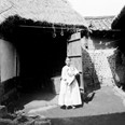Korejská křesťanka s dítětem v náručí stojící před přístodůlkem na dvoře usedlosti. Korea, Soul, 1901