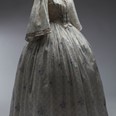 Šaty dámské bílé s drobným fialovým květinovým vzorem, tištěné jemné bavlněné plátno – mušelín, 1850–1860. Šaty pravděpodobně patřily principálce kočovné herecké společnosti Elišce Zöllnerové.